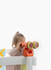 A little girl is looking through a pair of binoculars. White background.