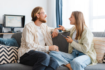 Cheerful couple relaxing on sofa using technology at home, talking
