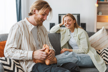 Man and woman sitting on a couch. Beautiful female smiling and the man is massaging her foot