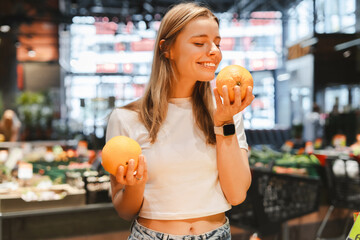 Young woman smelling oranges choosing goods in grocery store