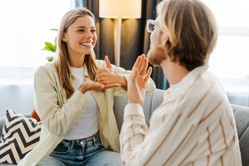 Happy, smiling couple, young man and woman communicating using sign language at home © Maria Vitkovska