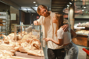 Happy couple choosing bread from bakery display in supermarket