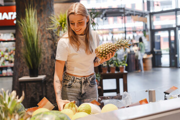 Young woman choosing ripe pineapple in grocery store