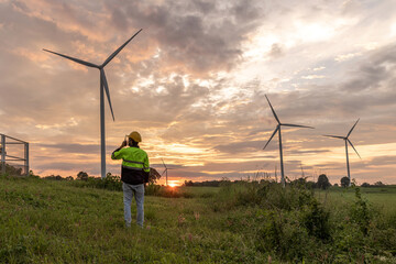 Professional Man Maintenance engineers working in wind turbine farm at sunset.  Engineer Man standing among Wind Energy Turbine. © kanpisut
