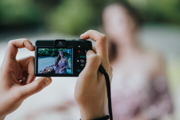 Hands holding a camera capturing an outdoor portrait of a woman. The viewfinder shows a woman in a...