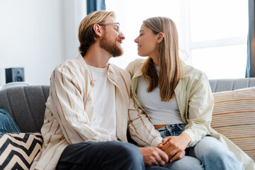 Young couple holding hands and looking at each other with love in living room, at home