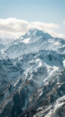 Obraz premium Snow-covered mountain range under a clear blue sky, featuring rugged peaks with varying shades of white and gray, and a few patches of dark forested areas.