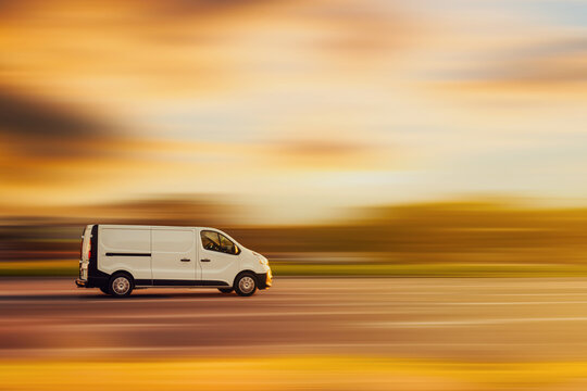 A white van is driving down the street at speed with a blurred background in the color of a yellow sunset. Concept of cargo transportation, goods delivery