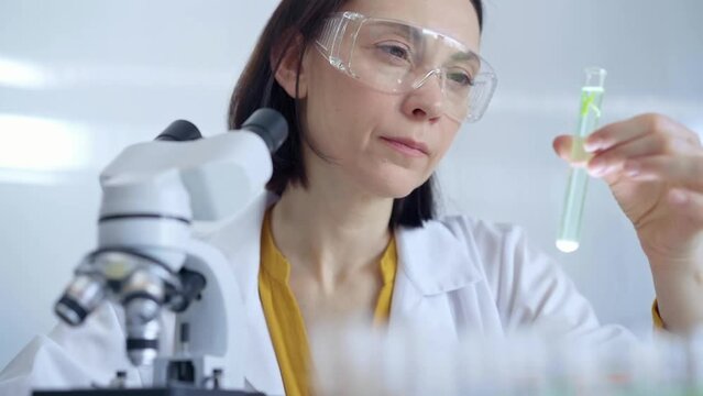 Scientist researcher with protective glasses examining lab tube with a green fluid. Microbiology and science concept