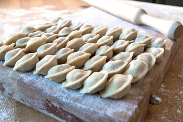 Raw dumplings were laid out on a wooden board for cooking. Next to it is a rolling pin for rolling out the dough. The filling is minced meat, potatoes, cheese or cottage cheese.