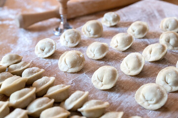 The raw dumplings were placed on a wooden cooking board. Next to it is a rolling pin for rolling out the dough and a tool for cutting the dough. Modeling dumplings by hand.