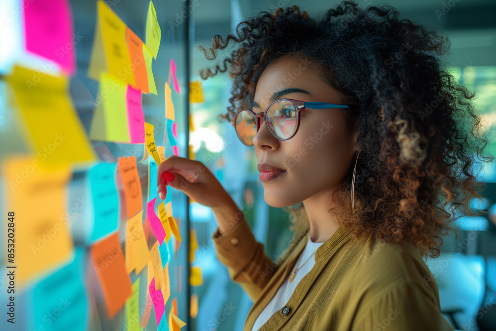 Poster a woman wearing glasses is looking at a board with colorful sticky notes on it. she is reaching out 