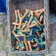 A variety of wooden souvenir slingshots in a wicker basket for sale at a fair.