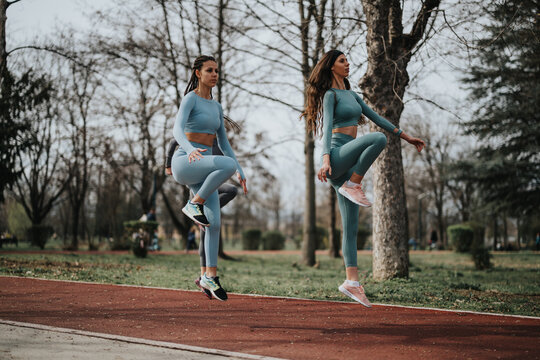 Two fit women in sportswear doing high-knee exercises outdoors on a sunny day, preparing for a workout. - Powered by Adobe