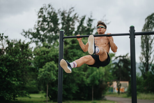 Athletic man exercising on parallel bars outdoors. Demonstrating strength and fitness, working out in a park setting surrounded by green trees.