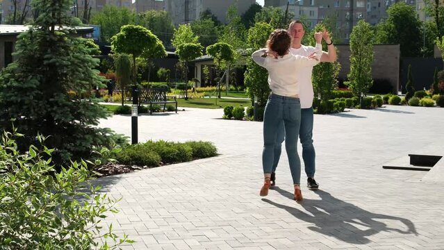 A young couple dances bachata in nature, a tall, strong man, a girl with curly hair, good-looking Europeans. Bachata outdoors
