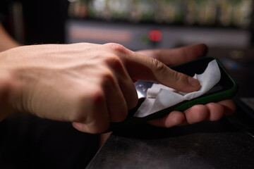 Ensuring hygiene, a person cleans a smartphone screen with a cloth for maintenance and safety