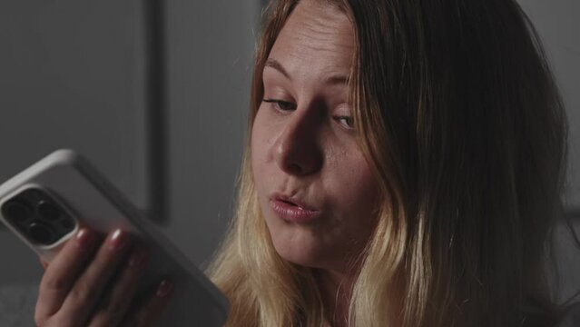 A young excited blonde girl uses a smartphone, holds the device, talks on speakerphone or video call, expresses pretentiousness with a surge of emotions and gesticulates with hand. The concept of