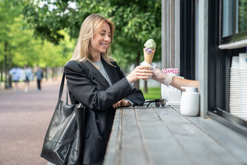 Contented woman buy ice cream in outdoor stand cafe, smiling takes waffle cone from window of stall...