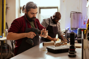 Woodworker next to african american coworker changing power drill head. Carpenter working with...