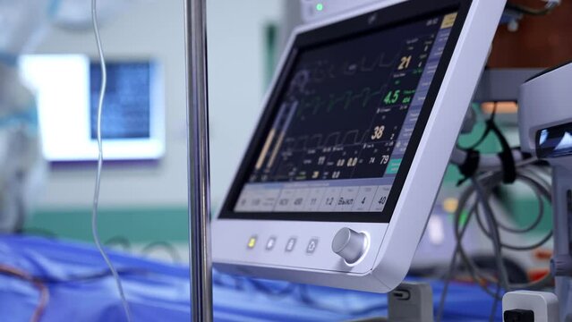 Side view of a screen with life parameters of a patient undergoing surgery. Equipment controlling condition of a person being operated. Close up. Blurred backdrop.