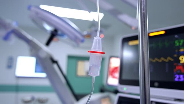 Drop counter reservoir hanging in the surgery room. Close up. Screens of lung ventilator work at backdrop.