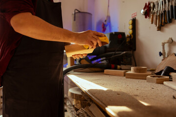 Woodworker in carpentry shop using sandpaper for sanding wooden surface before painting it, ensuring adequate finish. Woodworking specialist using abrasive sponge to fix damages suffered by wood
