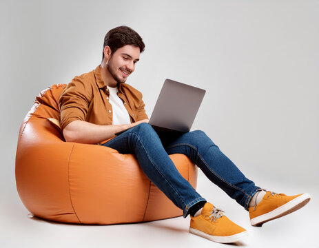 A man is sitting on a bean bag chair and using a laptop. He is smiling and he is enjoying himself. Concept of relaxation and leisure