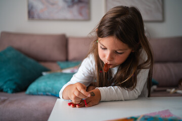 A young girl focuses on painting her nails while holding a chocolate treat in a cozy home environment
