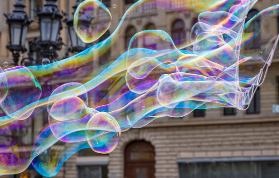 Many multicolored giant soap bubbles flying in the air on a windy day. Huge bubble are stretching on the wind into long smoothy changing form without popping. Close up. Copy space. Selective focus.