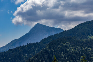 lunghi pendii verdi e alte cime montuose blu che si estendono in lontananza, di pomeriggio, in primavera, sotto un cielo azzurro e nuvoloso ed illuminati dal sole