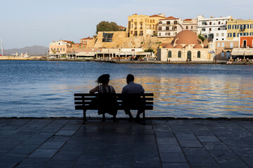 November 04, 2023. Europe, Greece, Crete, Chania harbor, old town. Man and woman silhouetted on a bench late in the day. Editorial use only.
