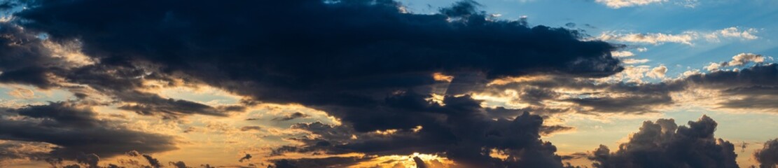 composizione panoramica da immagini multiple di un cielo nuvoloso, con tante grandi e piccole nuvole scure, in controluce, durante il tramonto