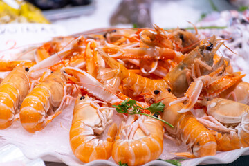 Assortment of fresh daily catch of prawns, seashells, molluscs on ice on fish market in Brittany, France, English translation: differens French names of seafood