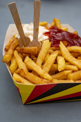 Belgian street and fast food, paper box in colors of Belgian flag with fried potato frit chips and ketchup and mayonnaise sauсe