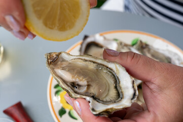 Hand with fresh live oyster, with citron, bread, butter and white wine served at restaurant in...