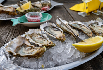 Eating of fresh live oysters with citron at farm cafe in oyster-farming village, Arcachon bay, Gujan-Mestras port, Bordeaux, France in sunny day, huge oyster