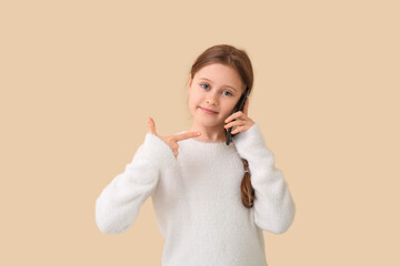 Little girl talking by mobile phone on beige background