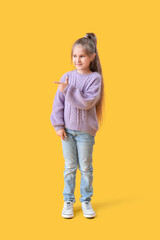 Cute little girl in knitted sweater pointing at something on yellow background
