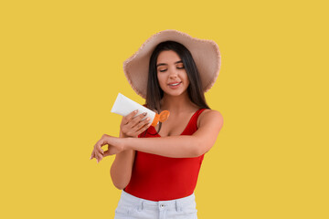 Beautiful young woman applying sunscreen cream on yellow background