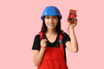 Young female electrician with multimeter on pink background