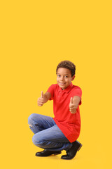 Little African-American boy showing thumbs-up on yellow background