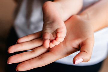 the parent's hand holds the baby's small leg, light close-up photo. family concept