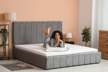 Young African-American woman with pillow lying on soft mattress in bedroom