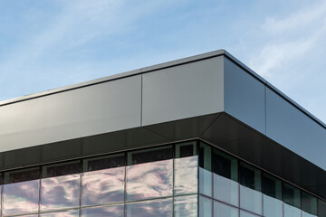 The exterior wall of a contemporary commercial-style building has aluminum metal composite panels and glass windows. The futuristic building has engineered diagonal cladding steel frame panels.