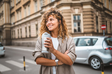 Adult beautiful woman stand on the street and hold thermos cup