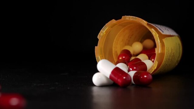 Close up of a prescription pill bottle tipping over with red and white pill capsules falling out. Concept for addiction, accidental poisoning, or overdose and suicide.