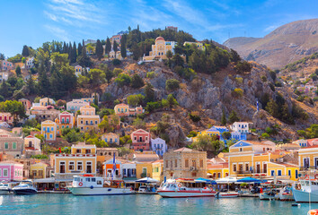 Naklejka premium Hillside view of the colorful buildings and busy harbor on Symi Island, Greece.