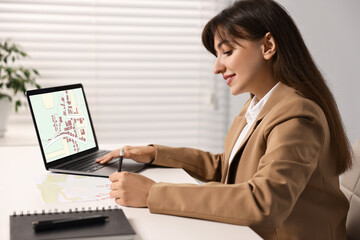 Woman working with cadastral map on laptop at table in office