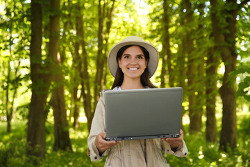 Forester with laptop examining plants in forest